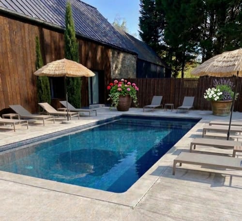 Le Manoir Des Haies à la piscine : bassin rectangulaire, chaises longues, parasols en chaume et bâtiments rustiques en bois