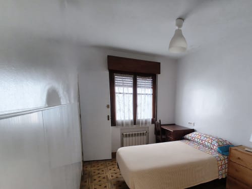 Acogedor dormitorio individual en Pensión Los Pinos Gijón con baño privado, cama de madera, ventana, radiador y ventilador de techo