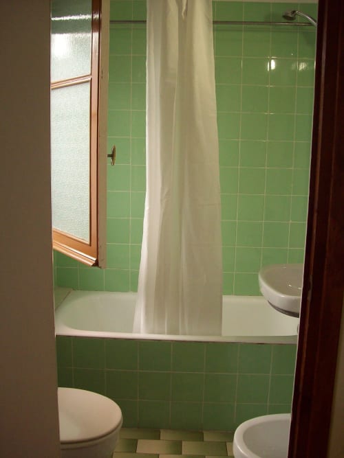 Baño con azulejos verdes, ducha con cortina e inodoro en Pensión Los Pinos Gijón