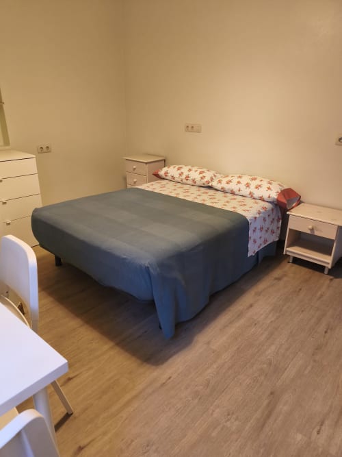 Habitación con cama de matrimonio en Pensión Los Pinos Gijón, paredes color crema, suelo de madera, mesita de noche y muebles blancos