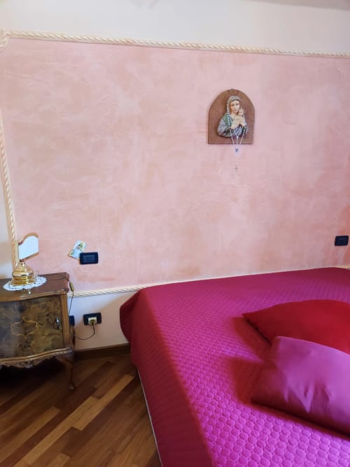 Suite Platone Prestige dell'hotel Gruppo Platone ad Alessandria, con pareti rosa, divano rosso e arredamento religioso