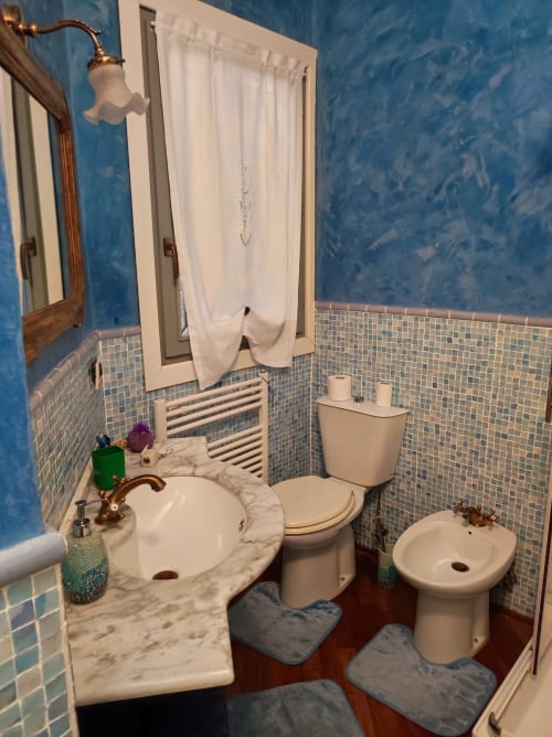 Bagno con piastrelle blu, lavabo in marmo, WC, bidet e rubinetteria in rame vintage presso l'hotel Gruppo Platone ad Alessandria