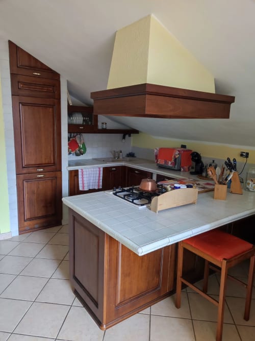 Cucina moderna con mobili in legno, isola attrezzata, fornello a gas e cappa color crema nell'appartamento di Alessandria