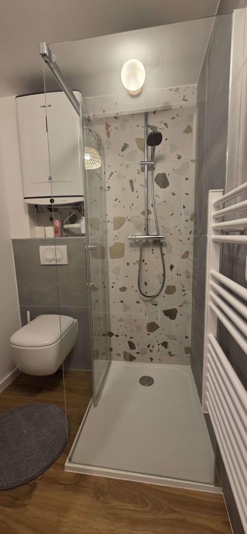 Salle de bains moderne avec douche à l'italienne, carrelage en terrazzo, toilettes murales, sèche-serviettes chauffant et miroir éclairé