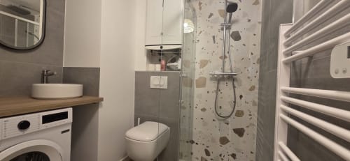 Salle de bains moderne de l'hôtel NN Patrimoine avec douche, toilettes, lavabo blanc, carreaux terrazzo et porte-serviettes chauffant