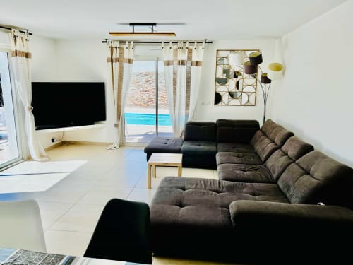 Salon de villa moderne avec canapé sombre, téléviseur écran plat et vue sur la piscine à Porto-Vecchio