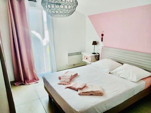 Chambre moderne de la villa Les Villas d'A Storia Porto-Vecchio avec mur d'accent rose, lit blanc et lustre perlé élégant