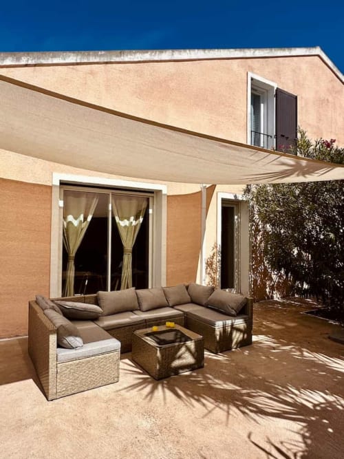 Salon de détente en rotin beige sous voile d'ombrage sur la terrasse des Villas d'A Storia, villa de luxe à Porto-Vecchio avec vue sur l'océan