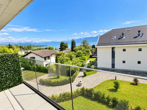 Balcony view at Attica Résidences St-Sulpice with lake and Alpine mountains, manicured gardens and modern buildings