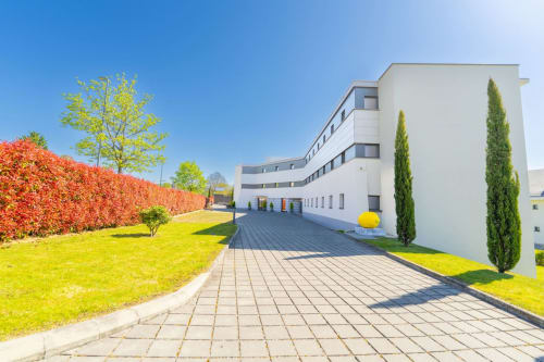 Attica Résidences St-Sulpice modern white building with manicured grounds, red hedge, and cypress trees