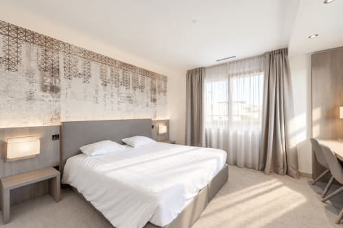 Modern hotel bedroom at Attica Résidences St-Sulpice with white bedding, gray headboard, and floor-to-ceiling windows