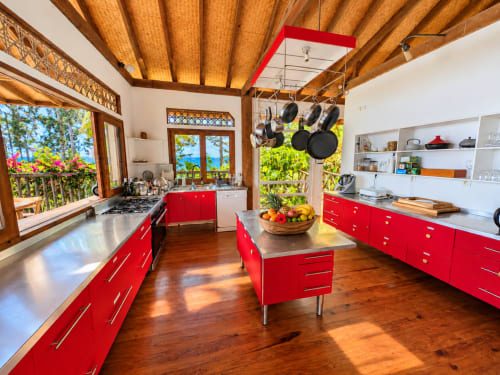 Cuisine rouge vif avec poutres en bois à Fare Tihi Moana, Tumaraa, comptoirs inox, îlot et vue sur l'océan