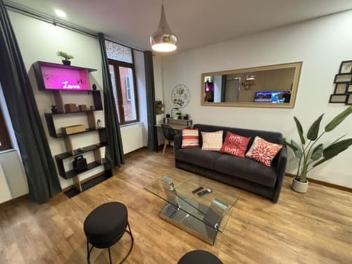 Salon moderne d'appartement à Annecy avec canapé noir, table en verre, étagères et luminaires suspendus