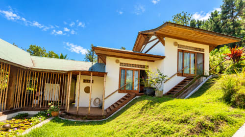 Cottage Fare Tihi Moana à Tumaraa avec terrasse en bois, murs blancs et jardins verdoyants sous un ciel bleu