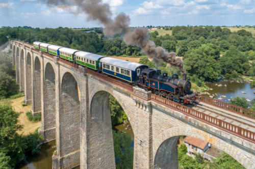 Train à vapeur traversant un viaduc en pierre près de Pouzauges, France avec la campagne et la rivière en contrebas