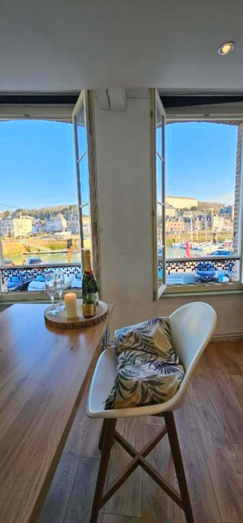 Appartement moderne avec fauteuil blanc face aux baies vitrées donnant sur le port de Saint-Valery-en-Caux et les bâtiments de la ville côtière