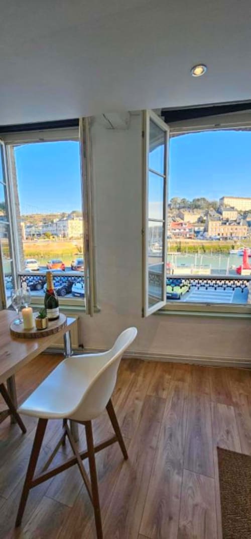 Appartement moderne aux fenêtres ouvertes donnant sur le port de Saint-Valery-en-Caux, coin repas avec bouteille de champagne