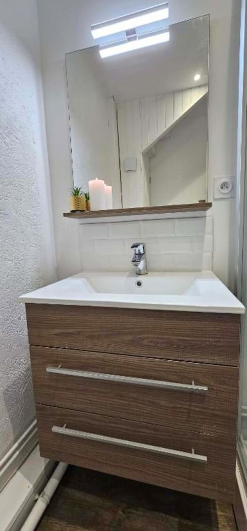 Salle de bain moderne avec meuble de lavabo en bois, lavabo blanc, miroir éclairé LED et bougie décorativeau Gîtes Saint Valery En Caux