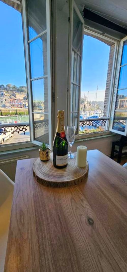 Bouteille de champagne et verre sur table en bois, vue sur le port de Saint-Valery-en-Caux et voiliers depuis les fenêtres ouvertes de l'appartement