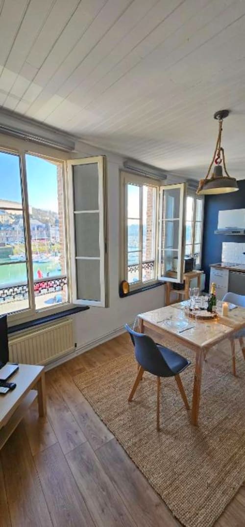 Salle à manger lumineuse avec baies vitrées sur le port de Saint Valery En Caux, table en bois, chaises bleues, suspension