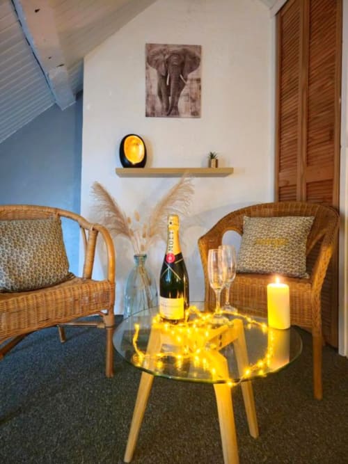 Cozy seating area in L'Atelier duplex apartment with wicker chairs, champagne bottle, fairy lights on glass table, and