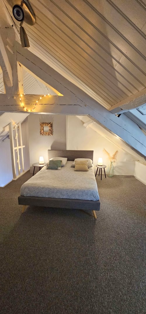 Cozy attic bedroom with sloped ceilings, queen bed, nightstands, warm lighting, and sea view at L'Atelier duplex in Saint