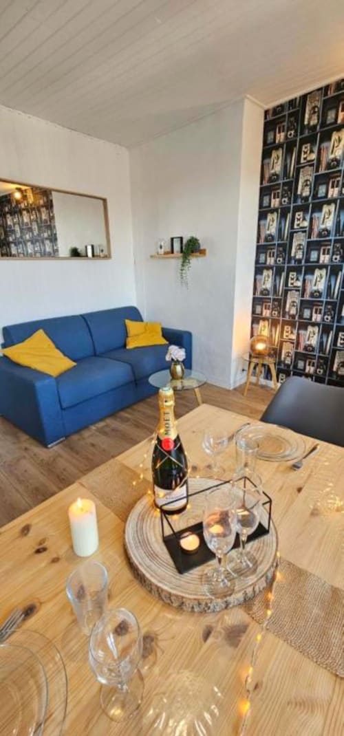 Modern apartment dining area with champagne bottle, blue sofa, and photo wall display at Gites Saint Valery En Caux