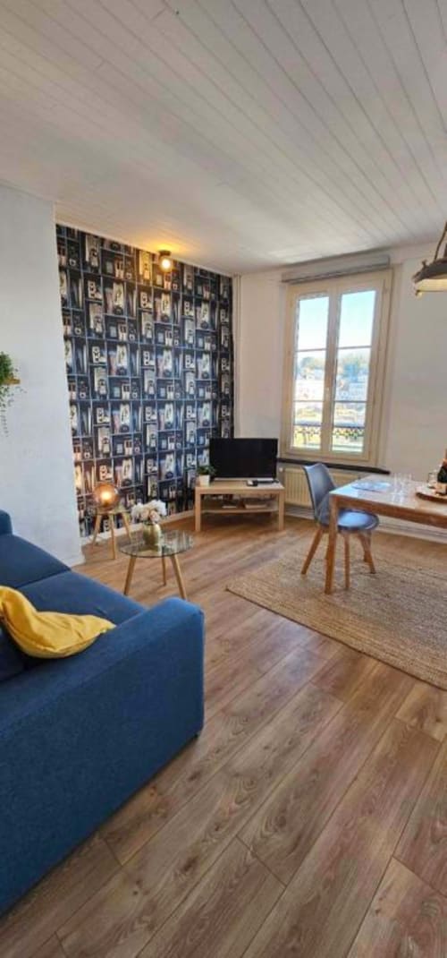 Modern duplex living room with blue sofa, navy patterned wall, wooden floors, desk area, and sea view through large windows