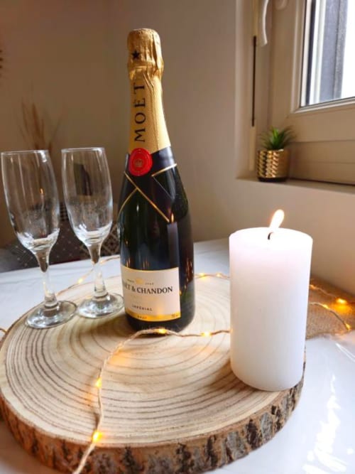 Elegant champagne setup with Moët & Chandon bottle, flute glasses, white candle, and warm lights on wooden coaster at Gites