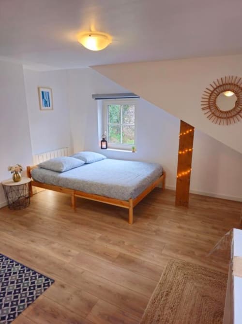 Modern attic bedroom at Gites Saint Valery with wooden bed, sloped ceiling, garden view window, and warm lighting in