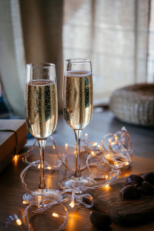 Two champagne flutes with sparkling wine and fairy lights on wooden table at Gites Saint Valery En Caux apartment