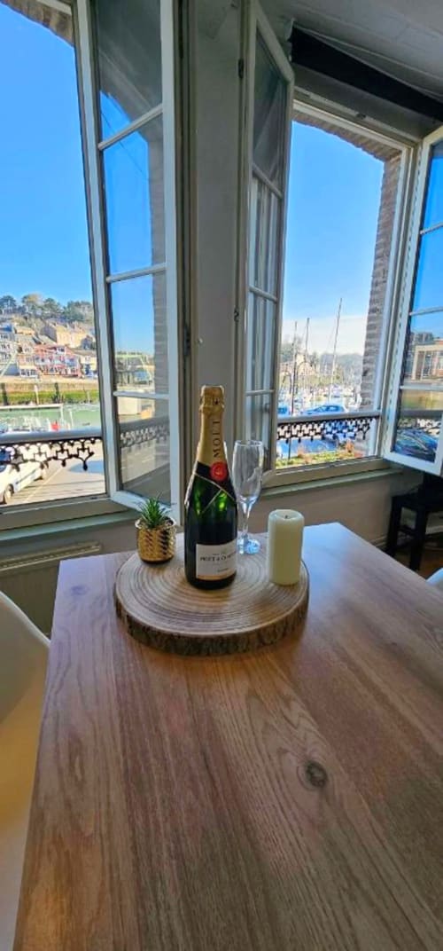 Bouteille de champagne et verre sur table en bois près de fenêtres ouvertes donnant sur le port de Saint-Valery-en-Caux