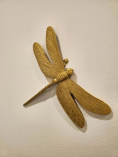 Décoration dorée en forme de libellule sur un mur clair.