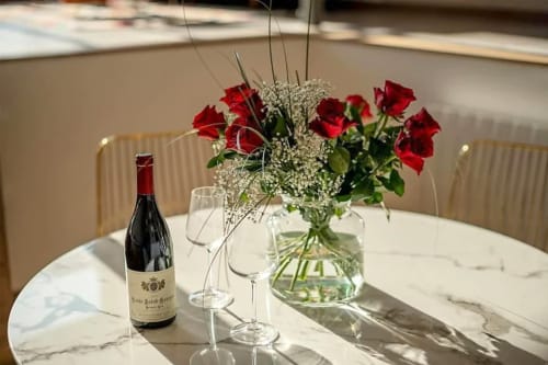 Élégant couvert de table aux Gîtes Saint Valery En Caux avec roses rouges, bouteille de vin et verres