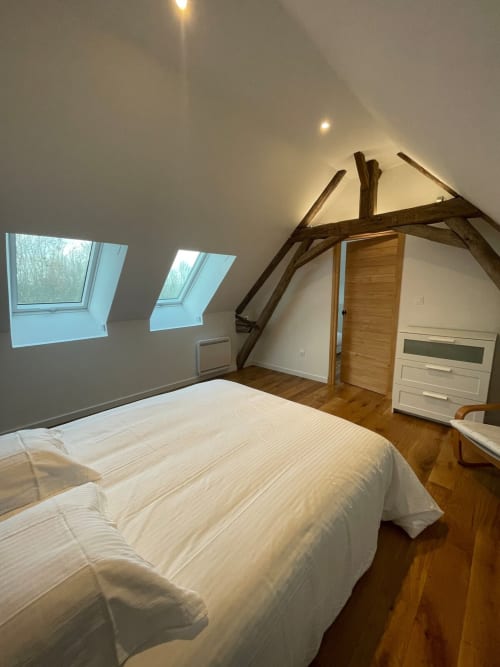 Chambre mansardée du gîte Molinet avec poutres apparentes, lucarne, literie blanche et parquet