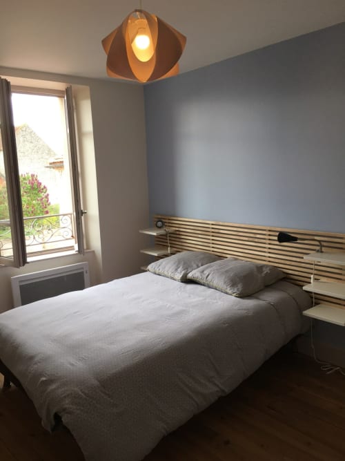 Chambre de cottage moderne à Molinet avec lit en bois, murs bleus, luminaire suspendu orange et balcon donnant sur les jardins
