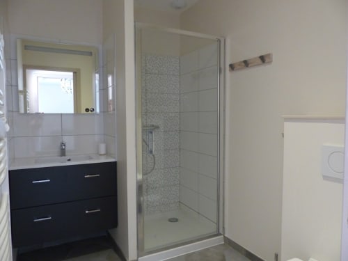Salle de bains moderne du gîte Molinet avec vasque noire, miroir, douche vitrée et carrelage blanc