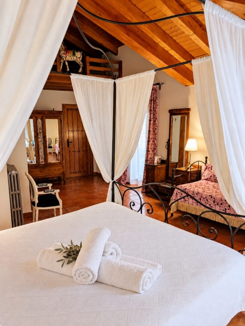 Dormitorio boutique de lujo con cama con dosel, ropa de cama blanca, vigas de madera y vistas a las montañas en El descanso del peregrino