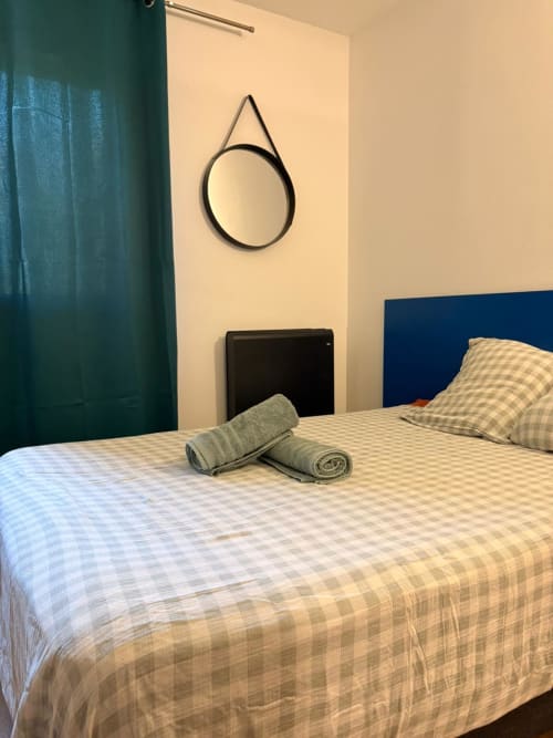 Chambre studio au Clos d'Aix à Aix-en-Provence avec tête de lit bleue, literie à carreaux, serviettes roulées et miroir rond