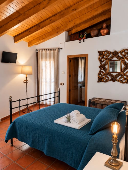 Habitación boutique en El descanso del peregrino con ropa de cama azul, vigas de madera y vistas a la montaña en Guadalupe, Cáceres