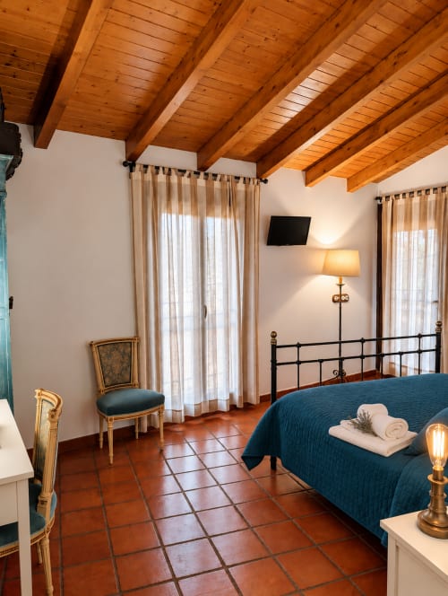 Dormitorio boutique en El descanso del peregrino en Guadalupe con vigas de madera, cama azul y vistas a la montaña