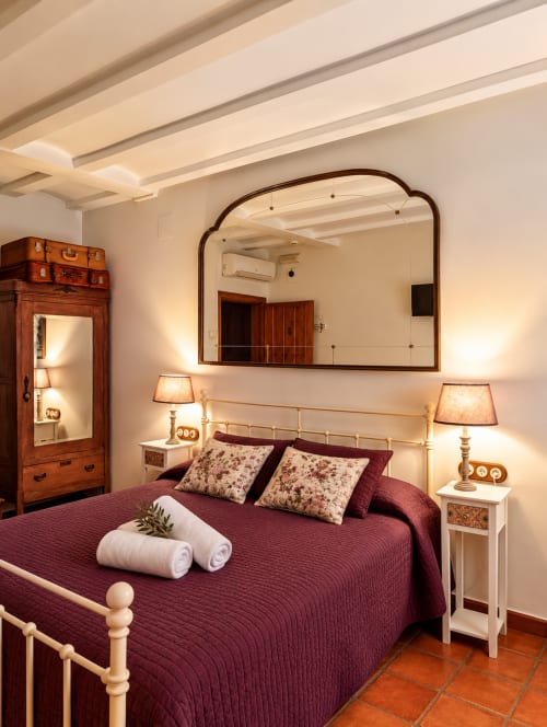 Dormitorio boutique en El descanso del peregrino de Guadalupe con ropa de cama burdeos, muebles de madera y espejo arqueado