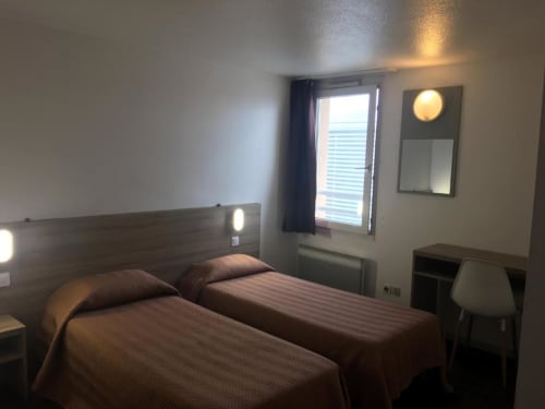 Chambre twin de l'hôtel Motelia à Moissy-Cramayel avec deux lits, tête de lit en bois, bureau et accès balcon