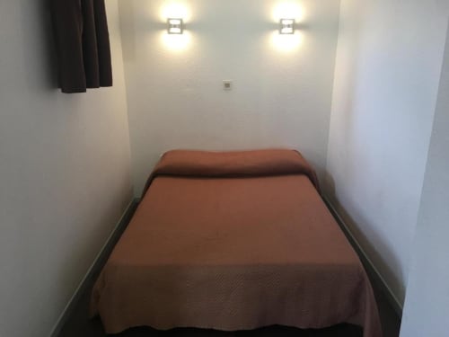 Chambre compacte à l'Hôtel Motelia avec lit, murs blancs et éclairage plafond