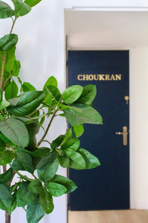 Porte de suite bleu foncé Choukran avec poignée en laiton, mur blanc et feuillage vert, entrée de l'hôtel Mi Casa Es Su Casa