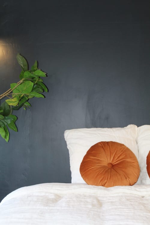 Chambre suite Mi Casa Es Su Casa Choukran avec coussin rond en terre cuite, literie blanche et plante verte sur mur bleu foncé