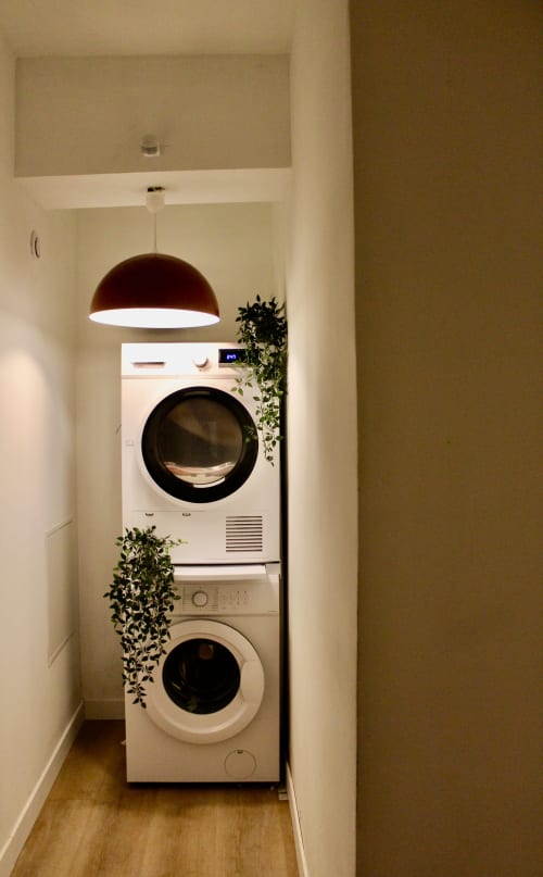 Buanderie moderne avec lave-linge et sèche-linge empilés, luminaire pendant bourgogne et plantes retombantes chez Mi Casa Es Su Casa