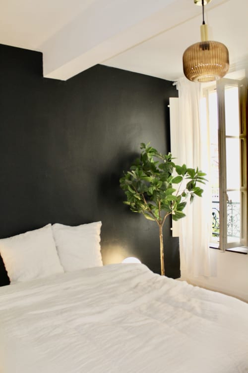 Chambre suite moderne avec mur d'accent noir, linge de lit blanc, plante en pot et luminaire doré suspendu à l'hôtel Mi Casa Es Su Casa
