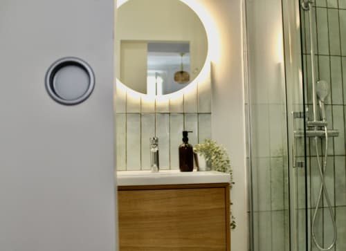 Salle de bain moderne avec miroir circulaire illuminé, meuble-lavabo en bois et douche vitrée dans la suite de l'hôtel Mi Casa Es Su Casa