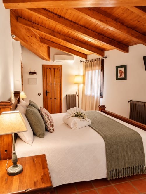 Dormitorio boutique en El descanso del peregrino, Guadalupe, Cáceres, con vigas de madera, ropa de cama blanca y decoración rústica